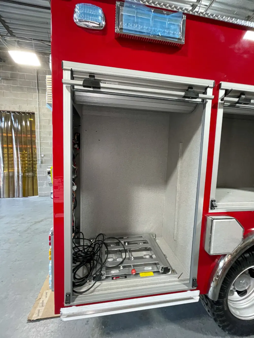 Exterior view of small fire truck showing cab, body compartments, and wheel/tire area.